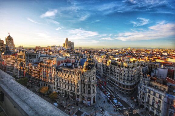 A panoramic view of Madrid, Spain, showcasing historic buildings and a sprawling cityscape against a dramatic sky at dusk.