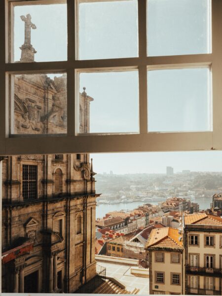 A view of Porto, Portugal, seen through a window, featuring historic buildings and a river in the distance.