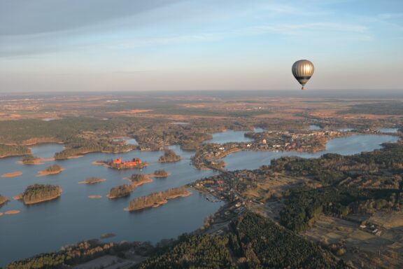 Aerial view of Trakai, Lithuania, featuring a landscape with multiple lakes and islands, with a hot air balloon floating in the sky.