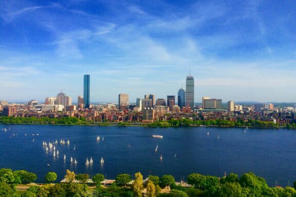 Aerial view of Boston, Massachusetts, showcasing the city skyline with buildings, greenery, and a river with boats.