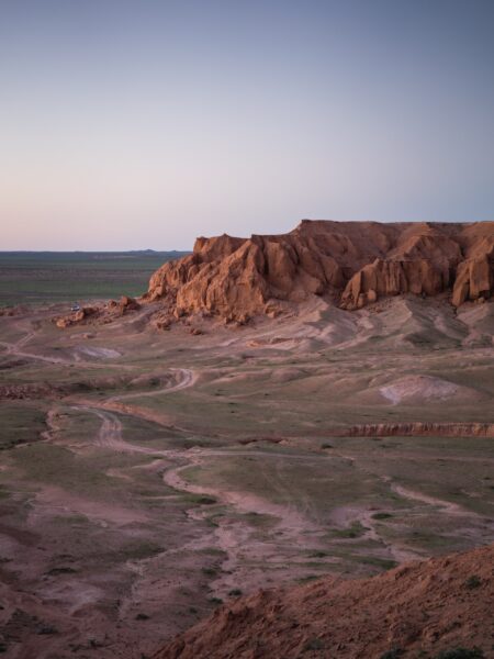 The image shows a peaceful scene in the Gobi Desert, Mongolia, with a pink sky over a barren landscape and a rocky horizon.