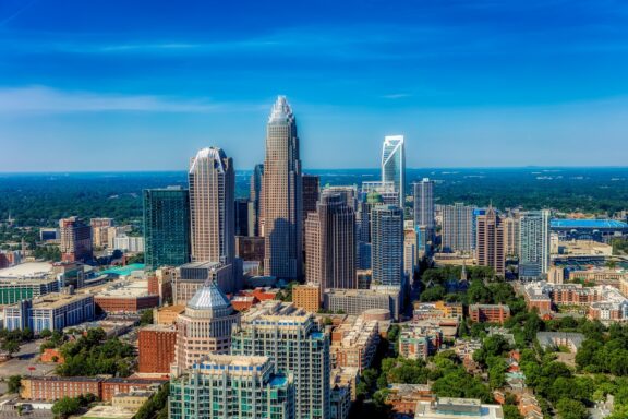 Aerial view of downtown Charlotte, North Carolina, showcasing skyscrapers and urban landscape under a clear blue sky.