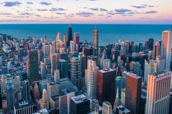 Aerial view of downtown Chicago, Illinois, showcasing the dense arrangement of skyscrapers and buildings at dusk with a colorful sky.