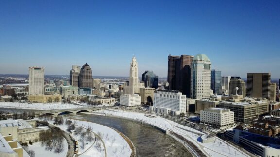 Aerial view of downtown Columbus, Ohio, with buildings and a river, in winter with snow cover.