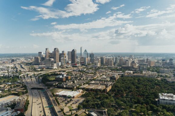 Aerial view of downtown Dallas, Texas with skyscrapers and a highway running through the city on a clear day.