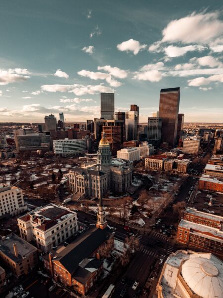 Aerial view of downtown Denver, Colorado, showcasing a mix of modern high-rise buildings and traditional architecture under a partly cloudy sky.