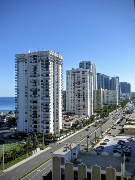 A view of high-rise buildings along a street in Hollywood, Florida, with a clear blue sky and the ocean in the background.