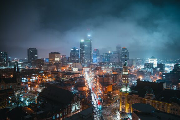 A nighttime cityscape of Indianapolis, Indiana, featuring illuminated buildings and streets with a hazy sky.