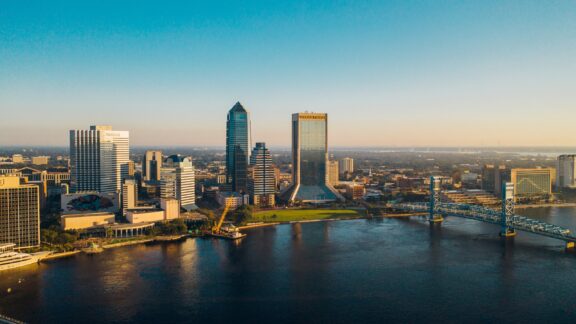 Aerial view of downtown Jacksonville, Florida, with skyscrapers and the St. Johns River at sunset.