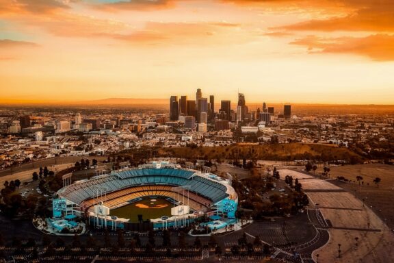 Aerial view of a stadium in the foreground with the Los Angeles city skyline in the background during sunset.