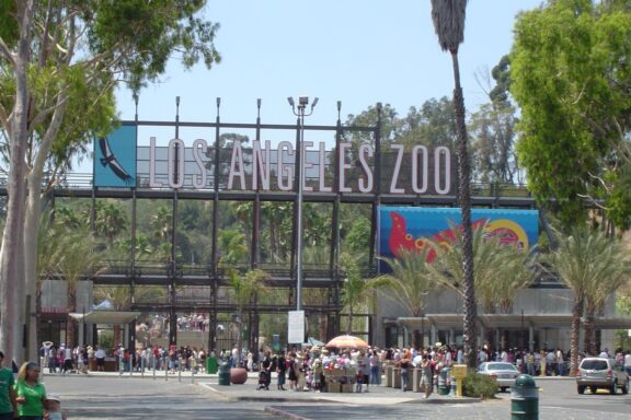 Entrance of the Los Angeles Zoo with a crowd of visitors and a large sign overhead.