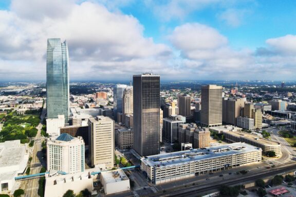 Aerial view of downtown Oklahoma City, Oklahoma, featuring skyscrapers, other buildings, and roads under a partly cloudy sky.