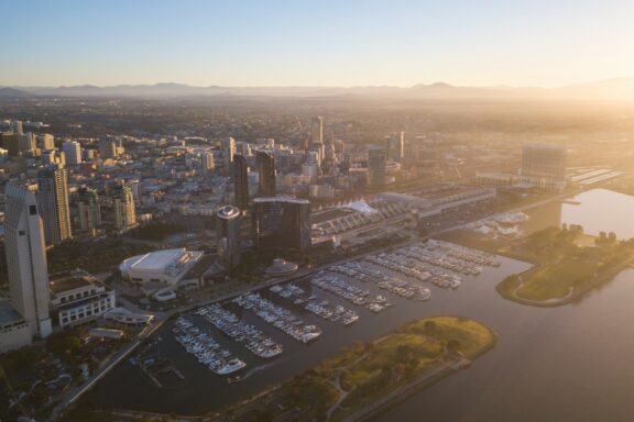 Aerial view of downtown San Diego, California during sunset with buildings, marina, and water visible.