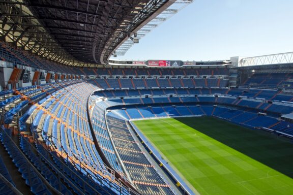 A view of the interior of Santiago Bernabeu Stadium with empty blue and orange seats under a clear sky.