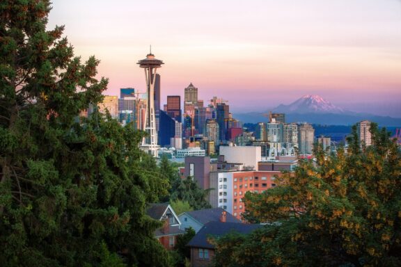 A view of Seattle, Washington, at dusk with the Space Needle prominent against a backdrop of city buildings and Mount Rainier in the distance.