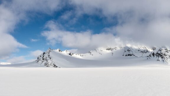 A sweeping view of the snowy Spitsbergen Arctic Desert, with mountains under a semi-cloudy sky.