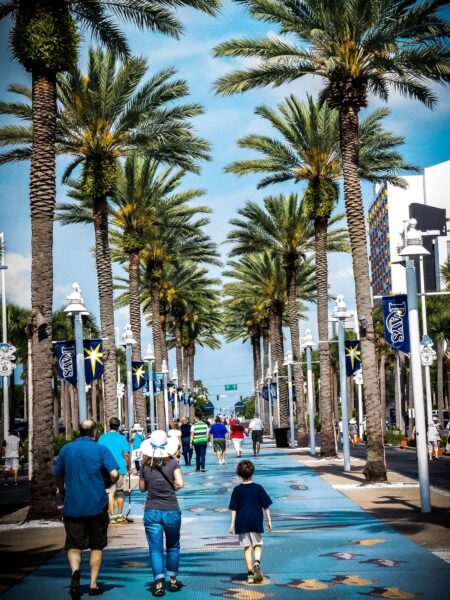 A sunny day in St. Petersburg, Florida, with people walking down a palm tree-lined street with blue pavement and festive decorations.