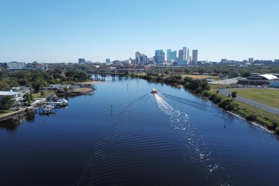 Aerial view of a body of water with a boat creating ripples, overlooking the skyline of Tampa, Florida, under a clear blue sky.