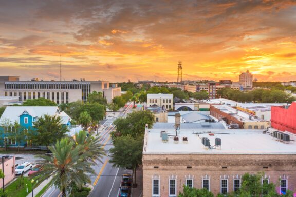 Aerial view of Gainesville, Florida at sunset with colorful sky, showcasing buildings and greenery.