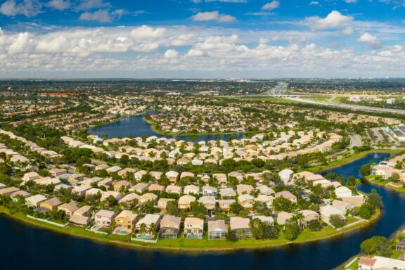 Aerial shot of a residential area in Pembroke Pines, Florida, with houses around a lake, greenery and a clear sky.