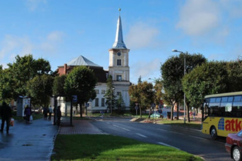 A street scene in Valga includes a church with a tall spire, a bus, pedestrians, and a partly cloudy sky.