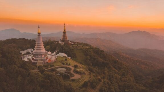 Aerial view of two ornate pagodas on the summit of Doi Inthanon with a background of mountainous landscape during sunset in Thailand.