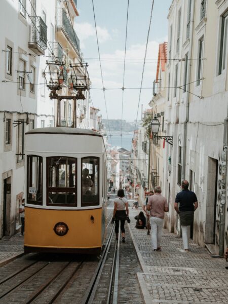 A traditional yellow tram on the streets of Lisbon, Portugal, with people walking nearby and buildings lining the street.