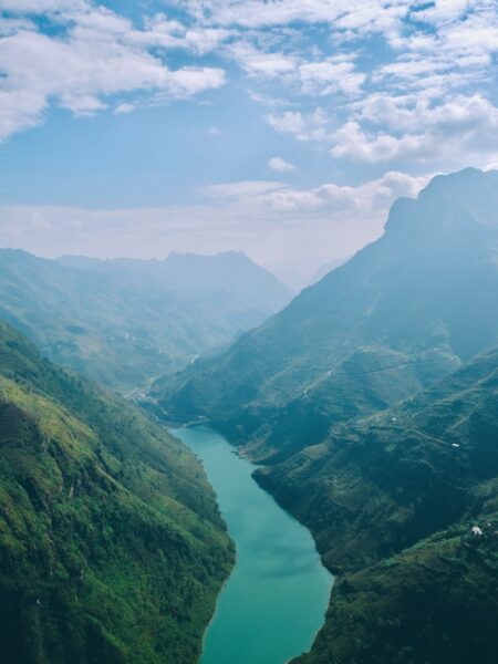 A picturesque view of Vietnam's Ma Pi Leng Pass, featuring a river in a valley, surrounded by green mountains under a blue sky.