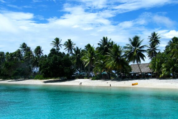 A tropical beach scene in the Marshall Islands with clear turquoise water, white sand, and lush green palm trees.