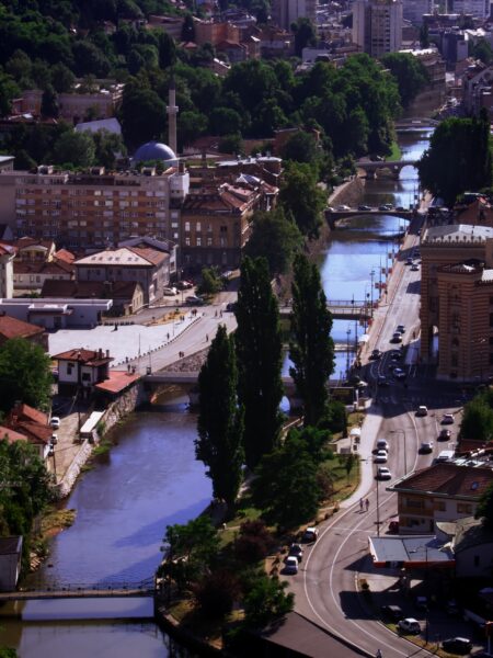 Aerial view of Sarajevo, Bosnia shows a river, bridges, buildings, and a mosque with a minaret.