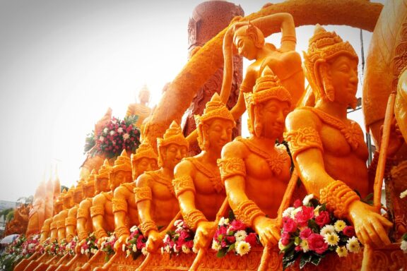 An image of intricately carved candles, possibly part of the Ubon Candle Festival in Northeastern Thailand, adorned with fresh flowers.