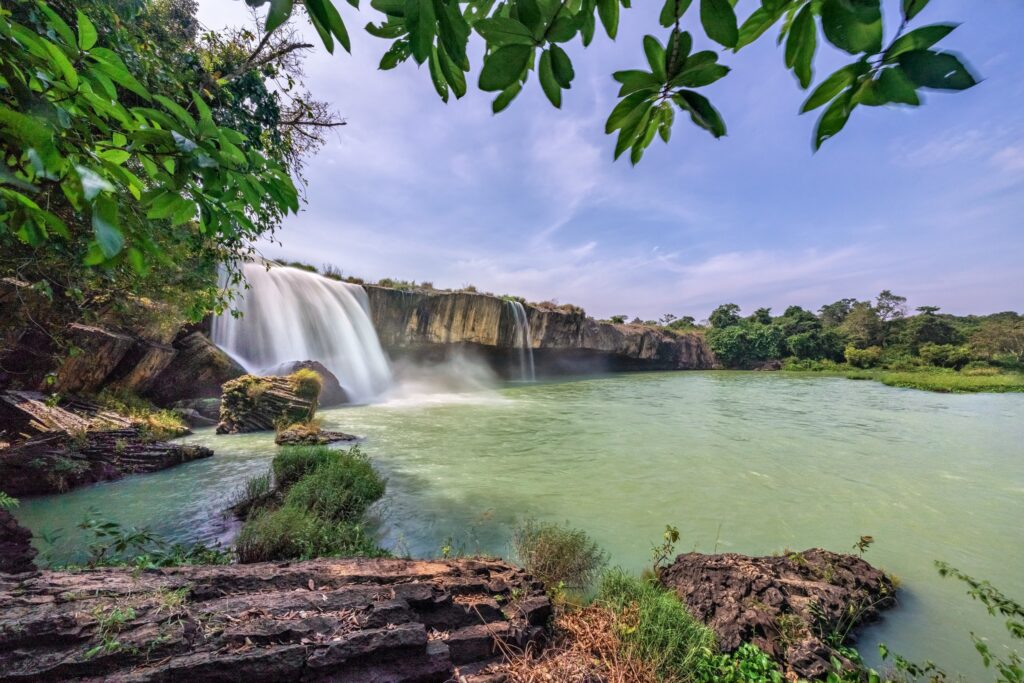 Dray Nur Waterfall in Vietnam offers a scenic view with cascading water, serene pool, lush greenery, and clear blue sky.