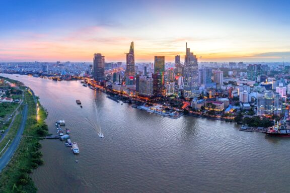 Aerial view of Ho Chi Minh City, Vietnam, during sunset with skyscrapers along the river and a colorful sky.