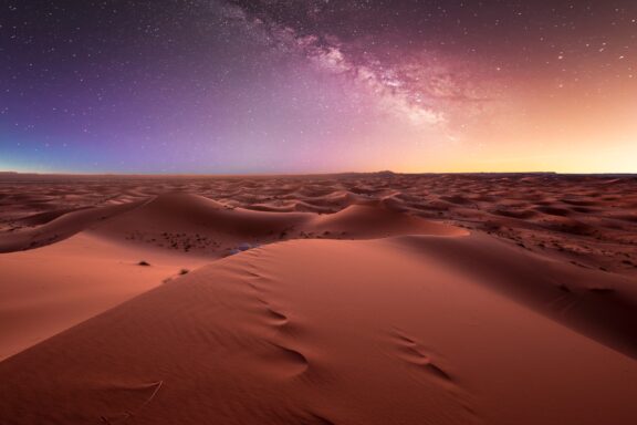 A starry sky with the Milky Way visible above sand dunes in Morocco.