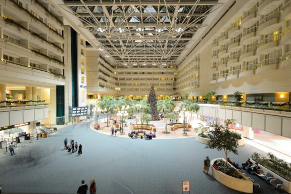 Interior view of Orlando International Airport with travelers, seating areas, and a central atrium with greenery.