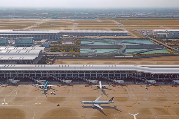 Aerial view of Shanghai Pudong International Airport with multiple airplanes at the gates and runways visible in the background.