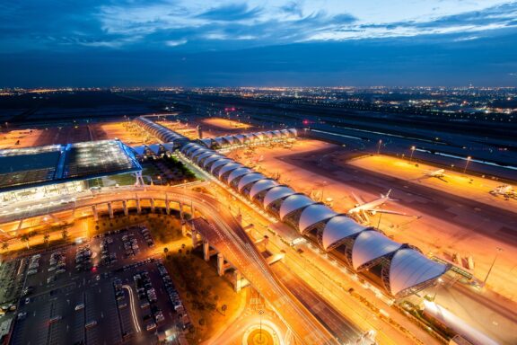 Aerial view of Suvarnabhumi Airport in Bangkok during twilight with illuminated terminals and runways.