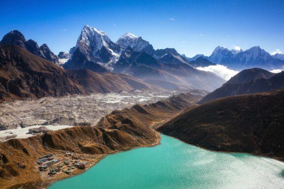 A panoramic view of Gokyo village by a turquoise lake with the Himalayan mountain range in the background, located in Nepal.