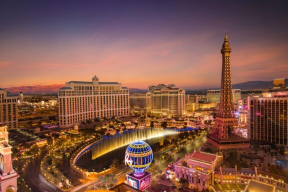 Aerial view of Las Vegas, Nevada at twilight with illuminated buildings and a replica of the Eiffel Tower visible.