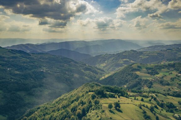 Aerial view of the rolling hills and lush greenery in Ovčinja, Serbia, with scattered clouds casting shadows on the landscape.