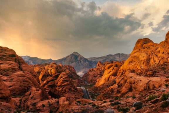 A scenic view of Red Rock Canyon, Nevada, featuring red rock formations under a dramatic sky with sunlight piercing through clouds.