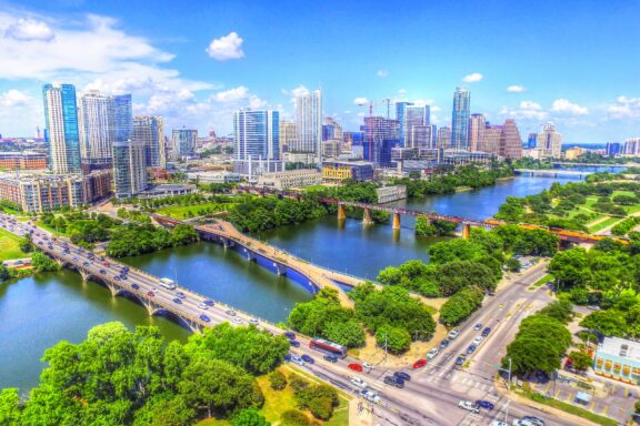 An aerial view of Austin, Texas showcases modern skyscrapers, a river, parks, and clear blue skies.