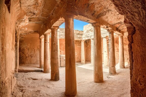 A view of the ancient Tombs of the Kings in Paphos, Cyprus, showing a series of stone columns within an underground chamber carved out of rock.