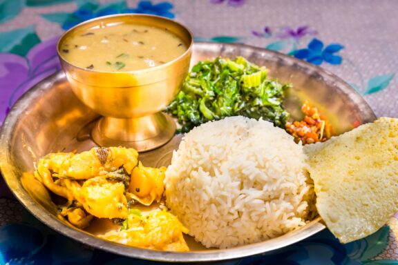 A traditional Nepali meal platter with dal bhat, which includes rice, lentil soup, vegetables, and a piece of flatbread, served on a metal plate.