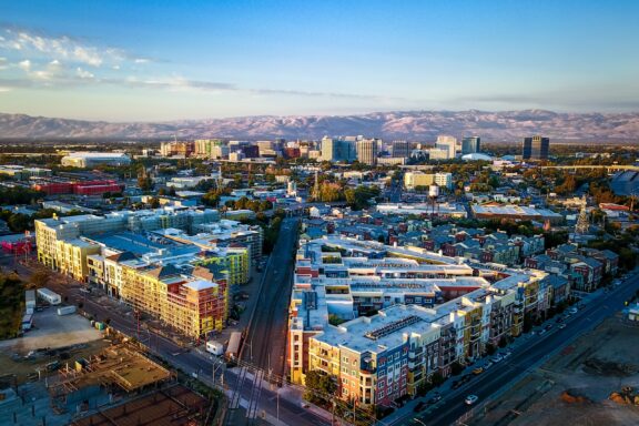 Aerial view of downtown San Jose with buildings, streets, and distant mountains under a clear sky.