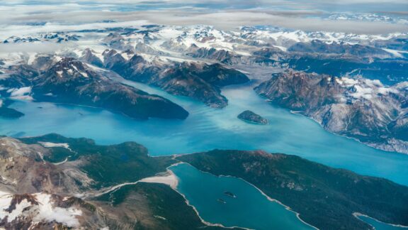 Aerial view of the fjords in Alaska with snow-capped mountains and turquoise waters.