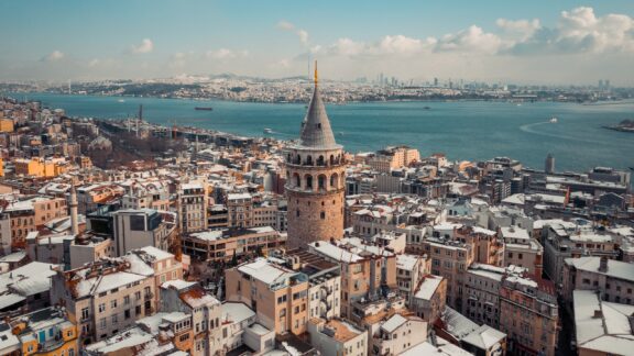 Aerial winter view of Istanbul, showcasing snow-clad buildings, Galata Tower, and the Bosphorus Strait.