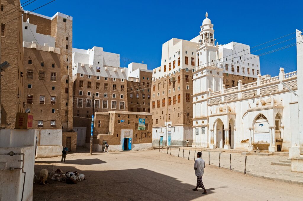 A person walking in a square surrounded by multistory traditional buildings with unique architectural details in Yemen.