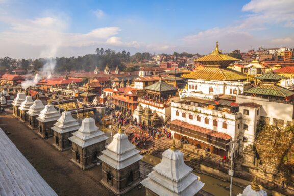 Aerial shot of Pashupatinath Temple in Kathmandu, showing tiered temples, rising smoke, and crowds.