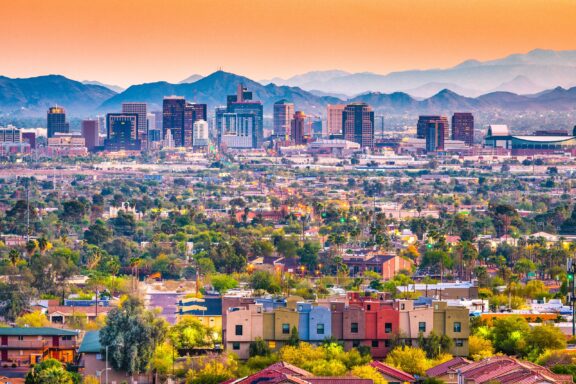 A colorful sunset view of downtown Phoenix, Arizona, with skyscrapers in the background and residential buildings in the foreground.